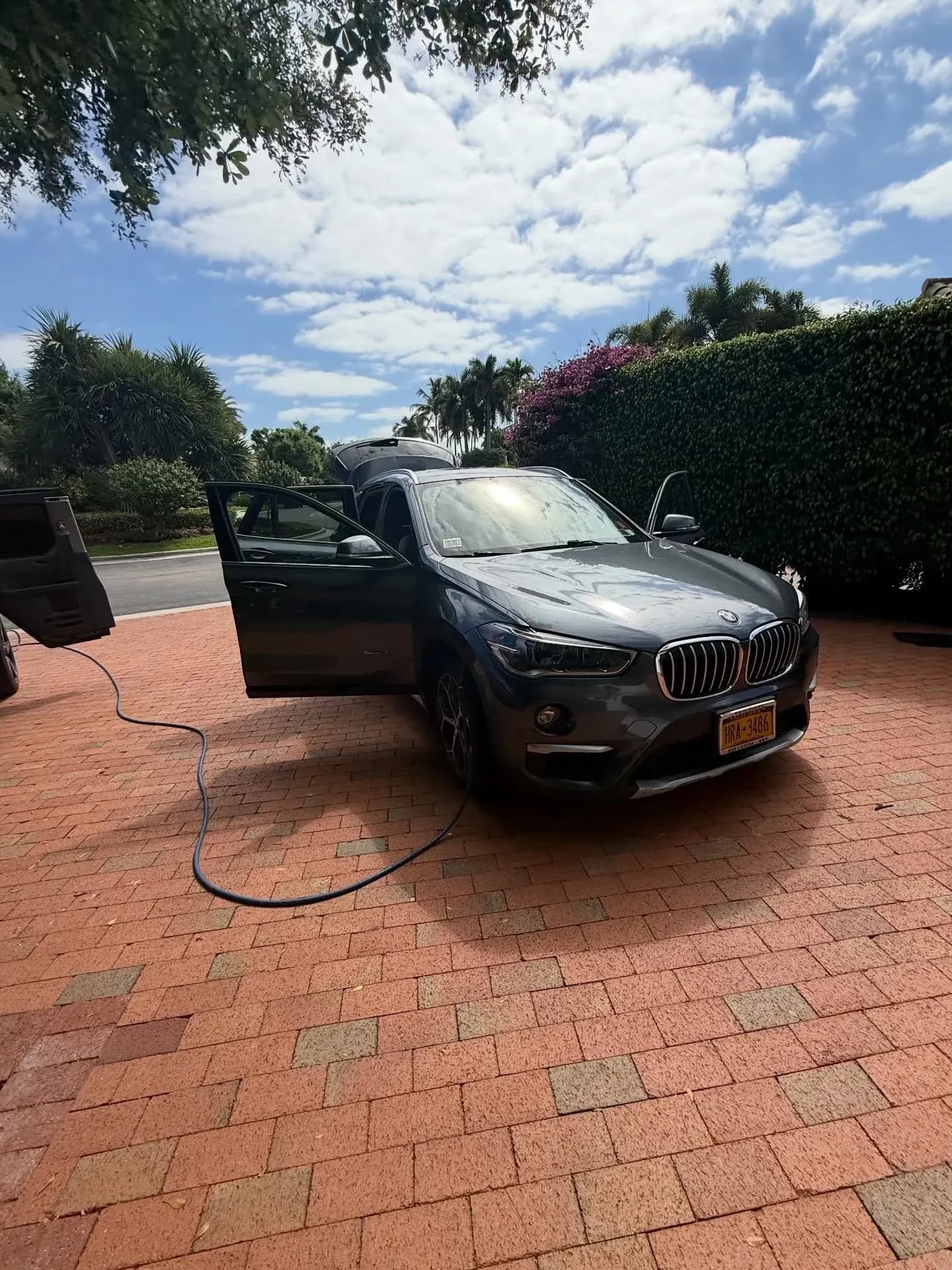 A gray BMW X1 with its doors open, mid-detail on a brick driveway